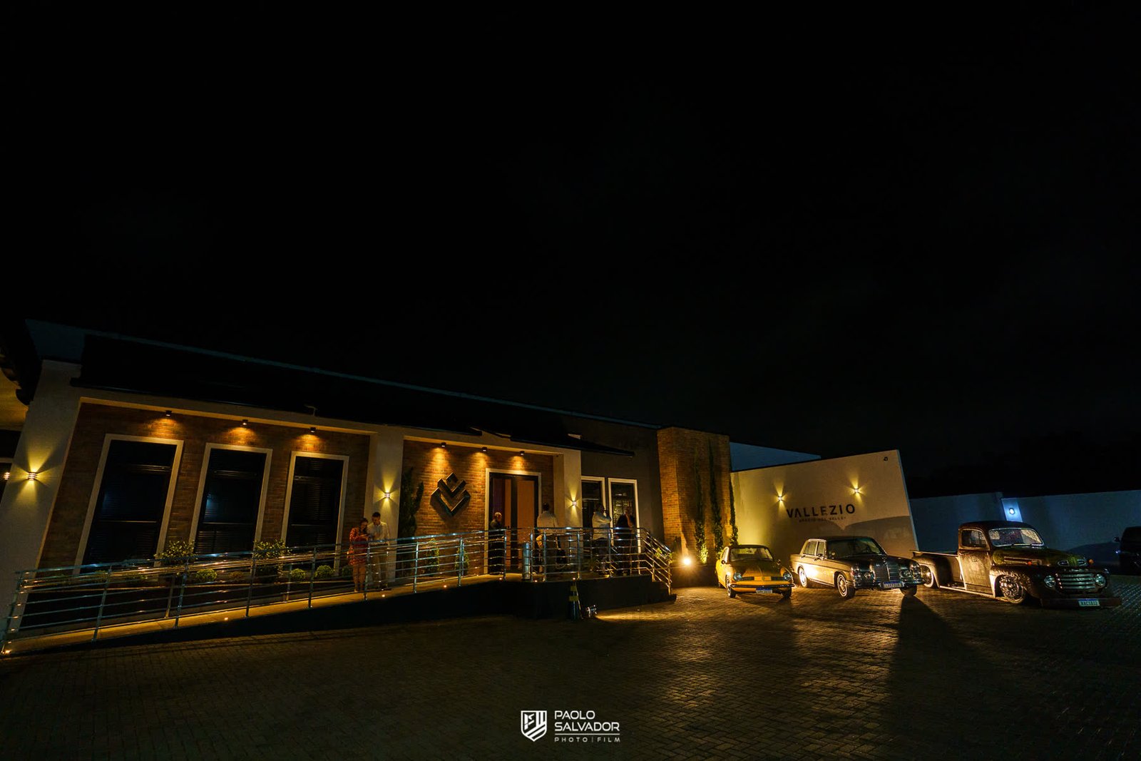 Fachada iluminada à noite, com carros antigos estacionados em frente
